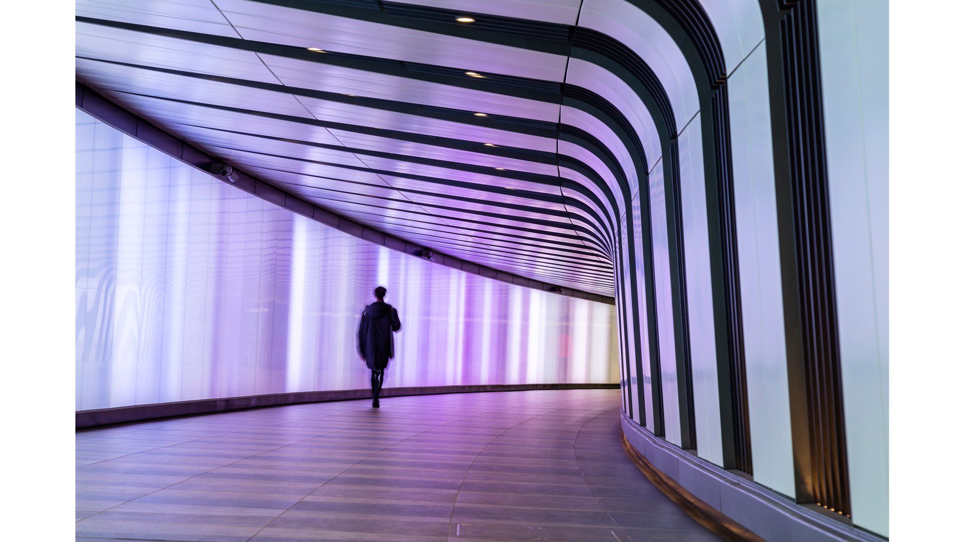 A person walks through a wide white and black tunnel with a purple light.